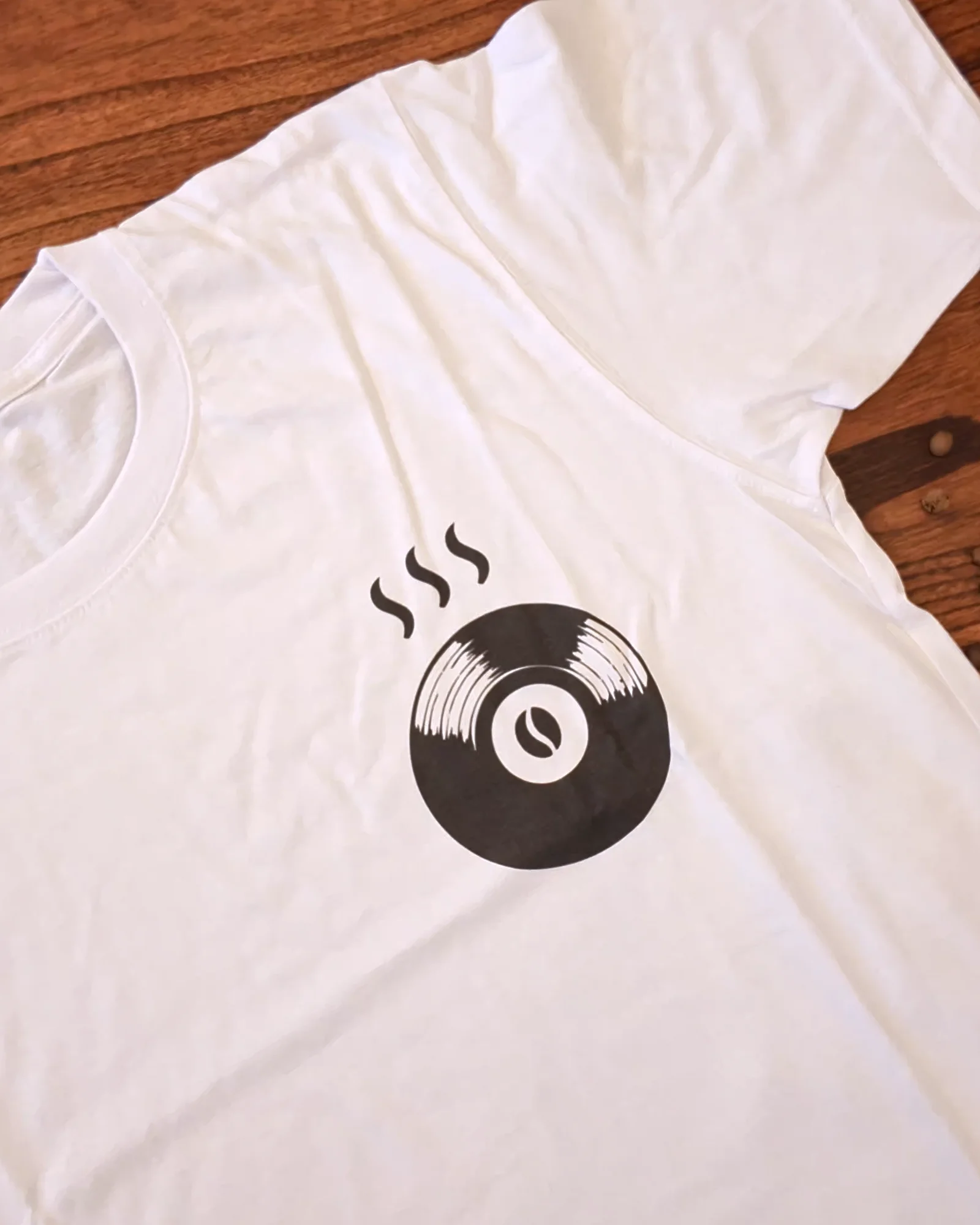 Remera blanca con el logo de Indómito en negro, sobre madera.